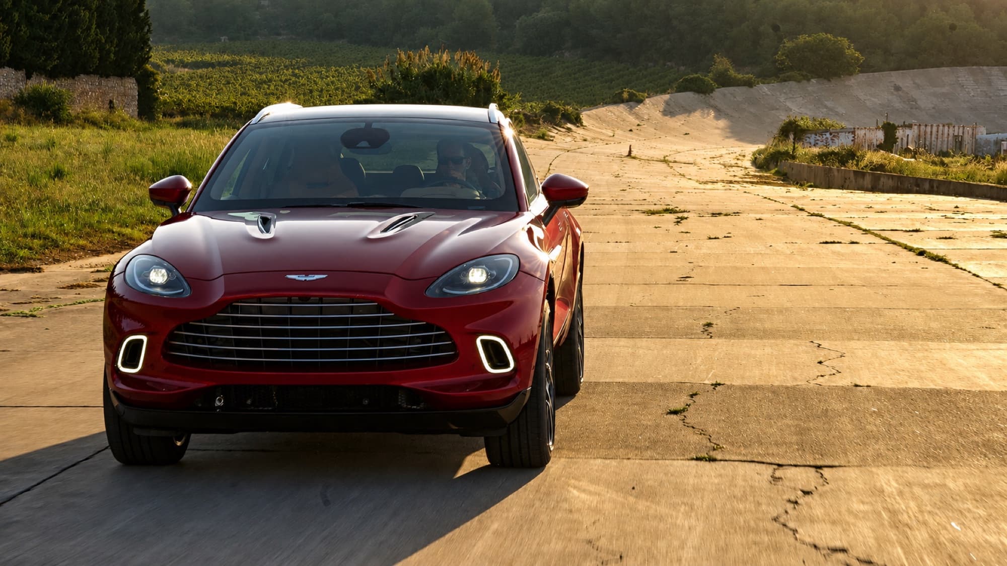 Red Aston Martin DBX on a golden-hour Spanish road — thousands of parts moving as one machine